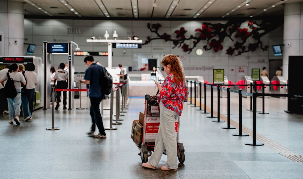 A traveler checks her phone while waiting with a luggage cart at a busy airport terminal in Guangzhou.