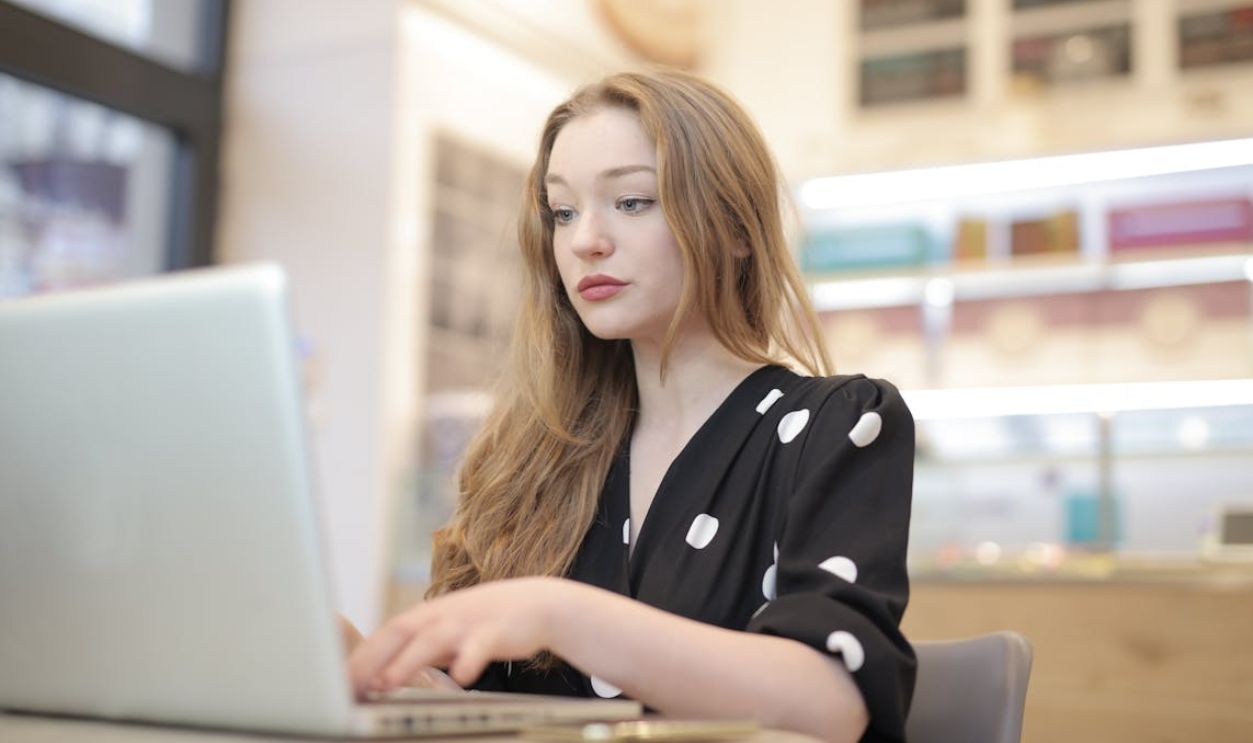 A young woman focuses on work as she types on her laptop in a bright, modern office setting.