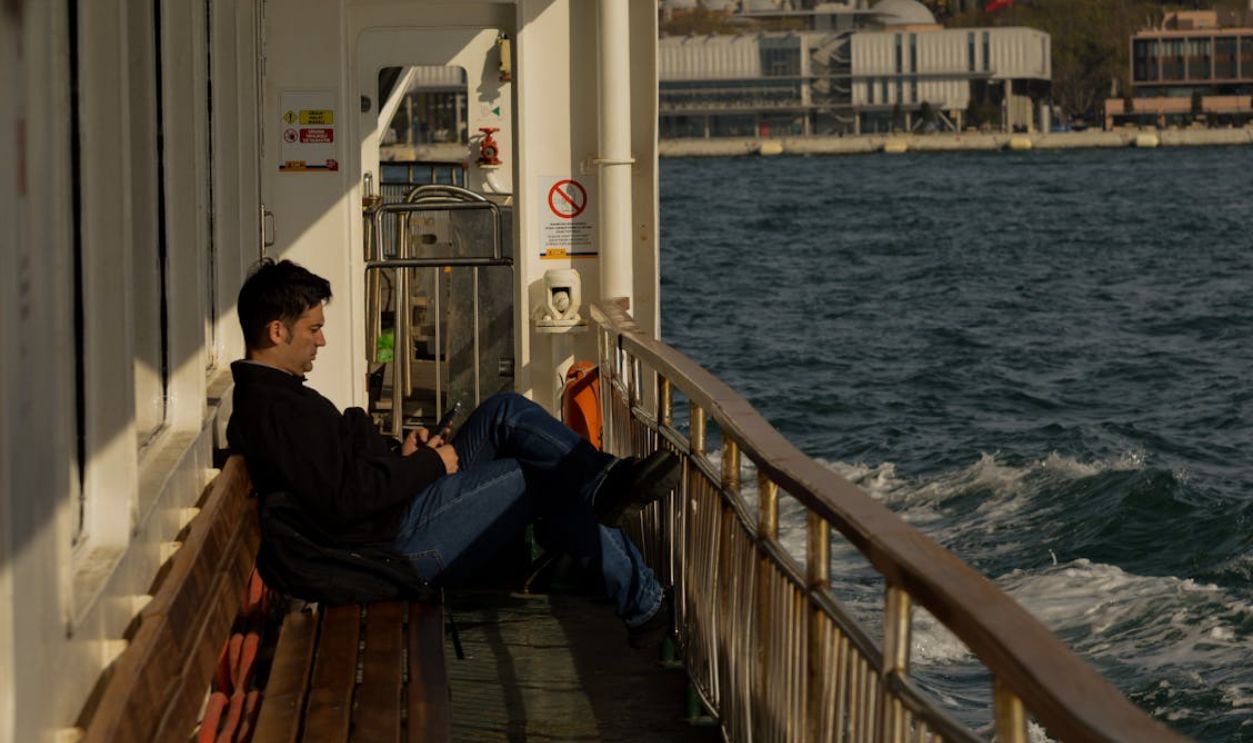 A man leans back on a ferry seat, enjoying the ocean view on a sunny day.