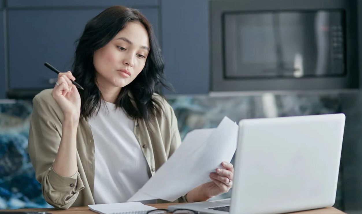 Young woman reviewing documents and working on a laptop in a modern home office setting.