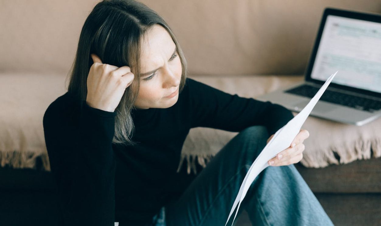 Focused woman analyzing papers with a laptop open, symbolizing thoughtful consideration.