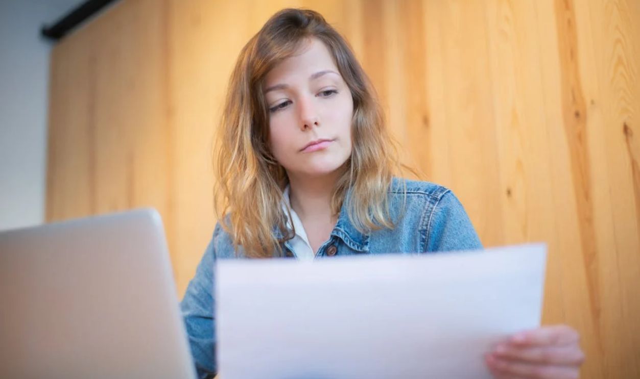 Businesswoman in a denim jacket analyzing documents at a wooden table in a cozy workspace.
