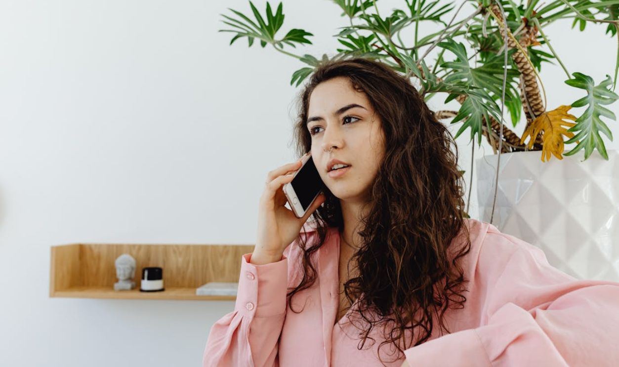 Confident young woman talking on smartphone in a modern interior with green plant background.