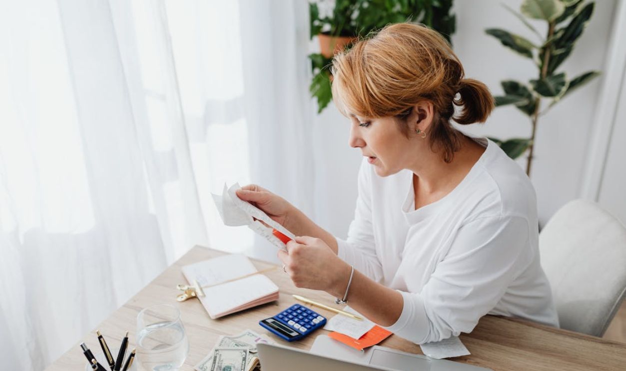 Woman sitting at a desk managing finances with a calculator and paper receipts in an office setting.