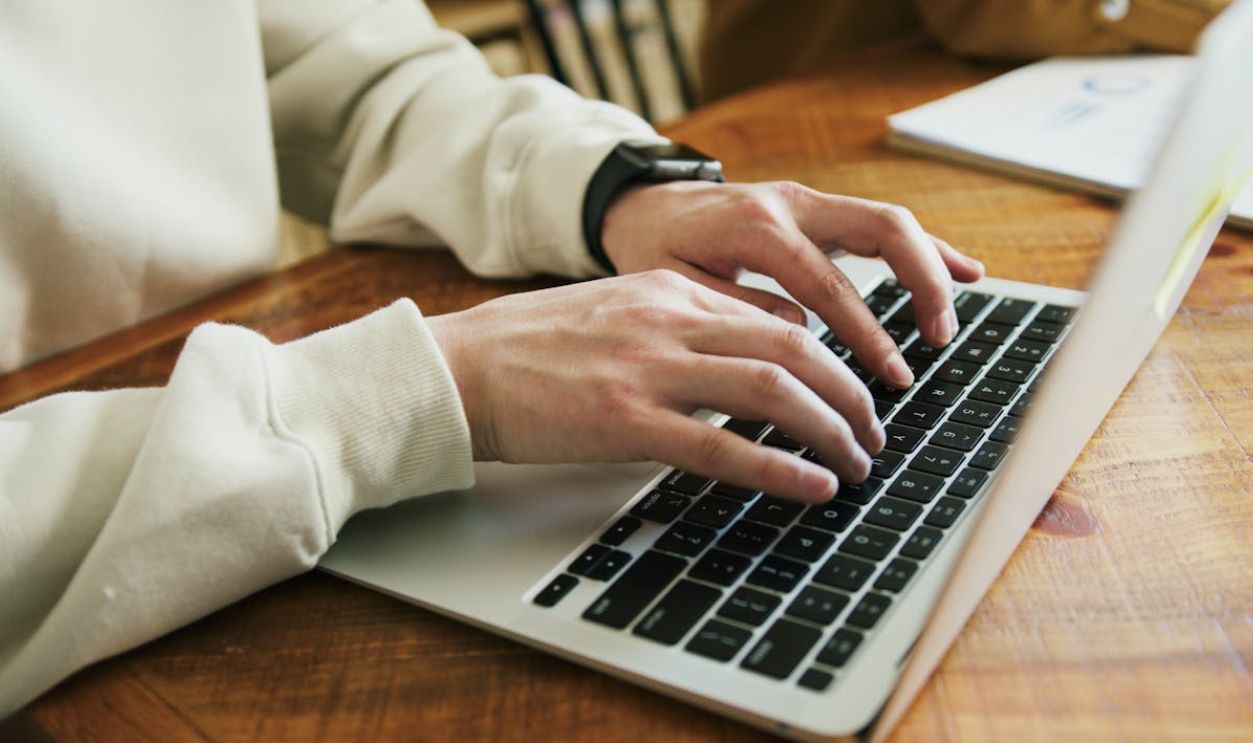Hands typing on a laptop keyboard on a wooden desk, close-up view.