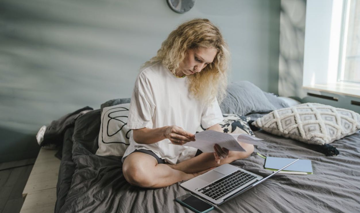 A woman working from home with a laptop and papers on her bed, enhancing comfort and productivity.