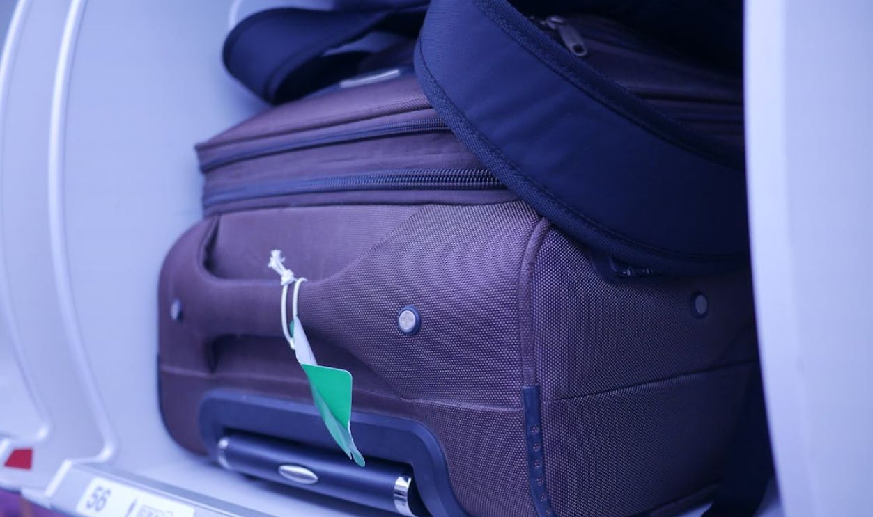 Close-up of luggage in an airplane's overhead compartment, showcasing travel essentials.