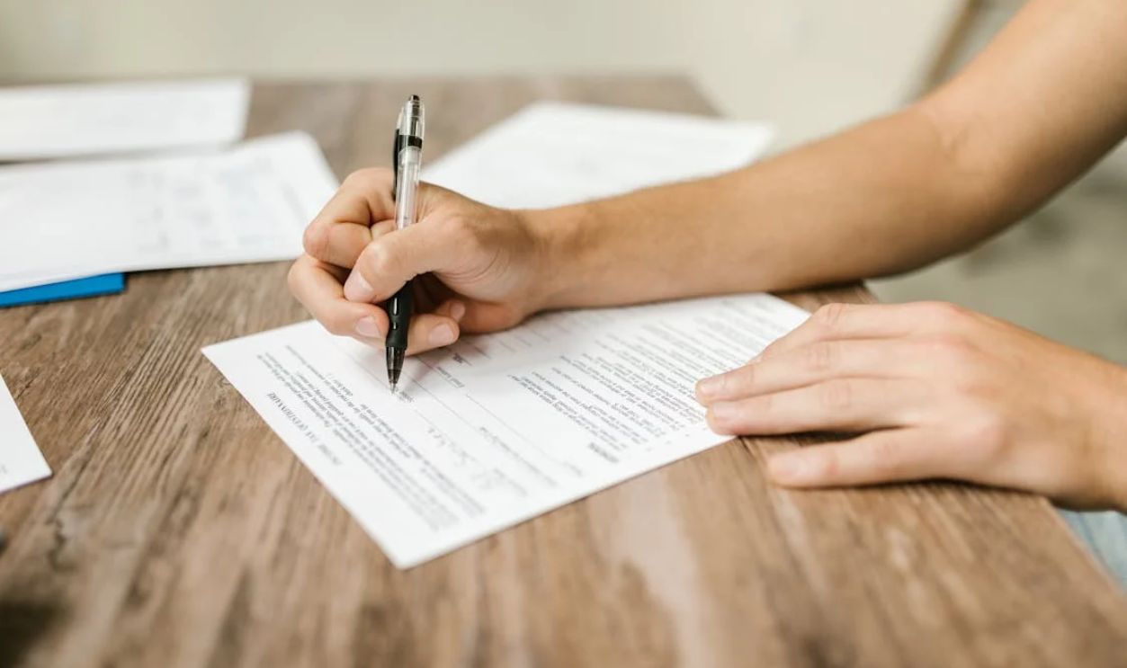 Hand filling out paperwork with a pen, showcasing focus on document completion.