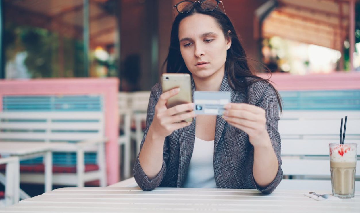 Woman using smartphone for online shopping at a cafe with credit card in hand.