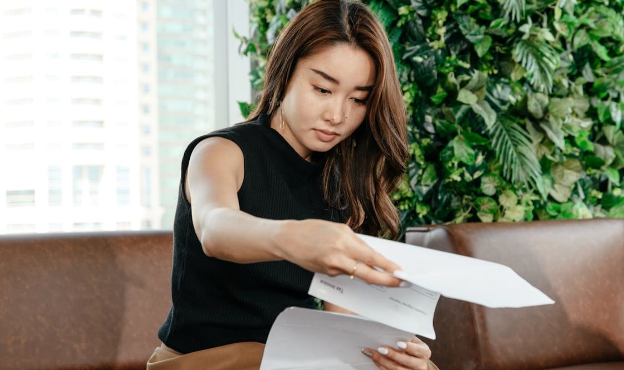An Asian woman focusing on paperwork in a modern indoor workspace, showcasing professionalism and efficiency.