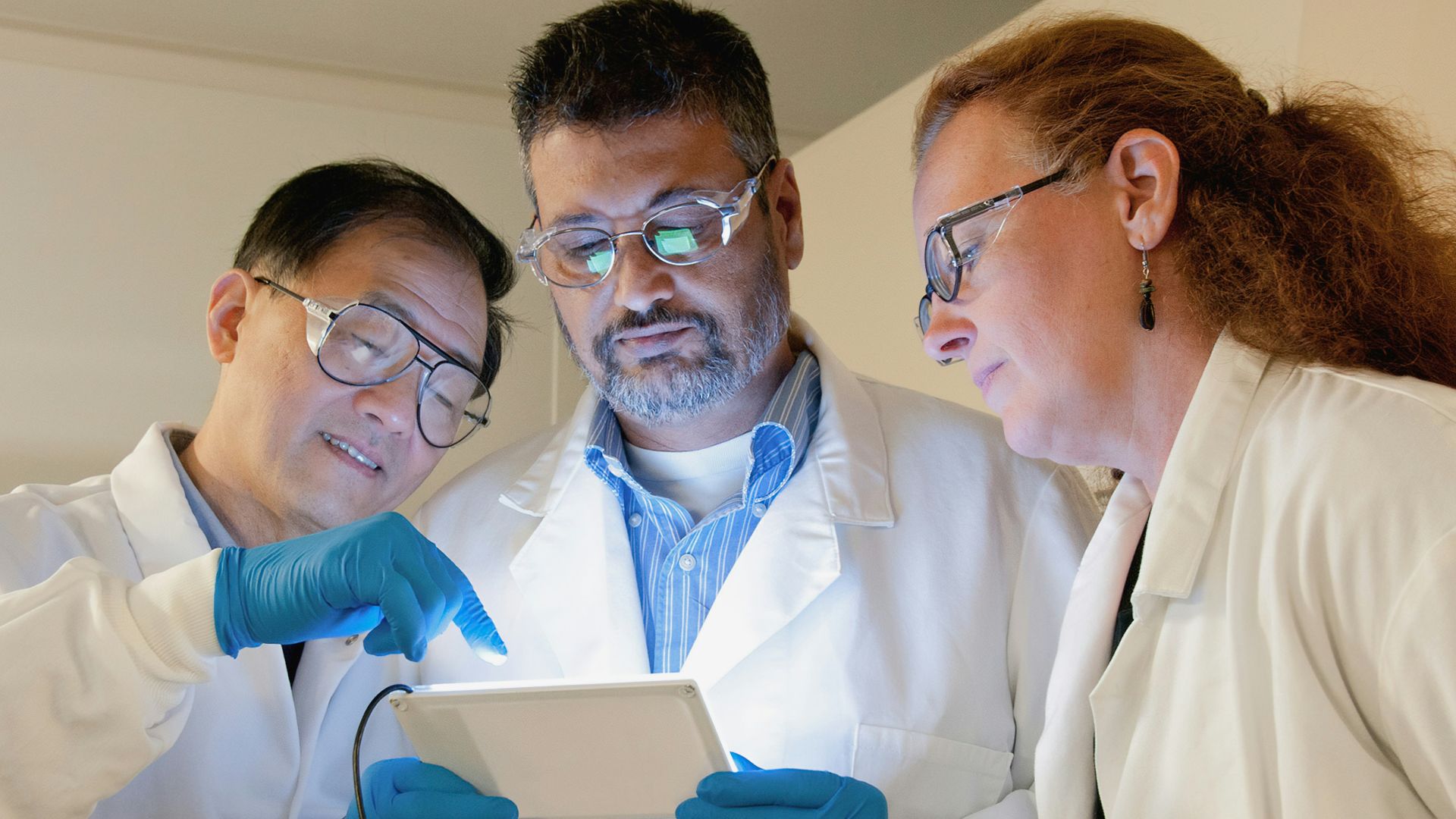 three people in lab coats looking at a tablet