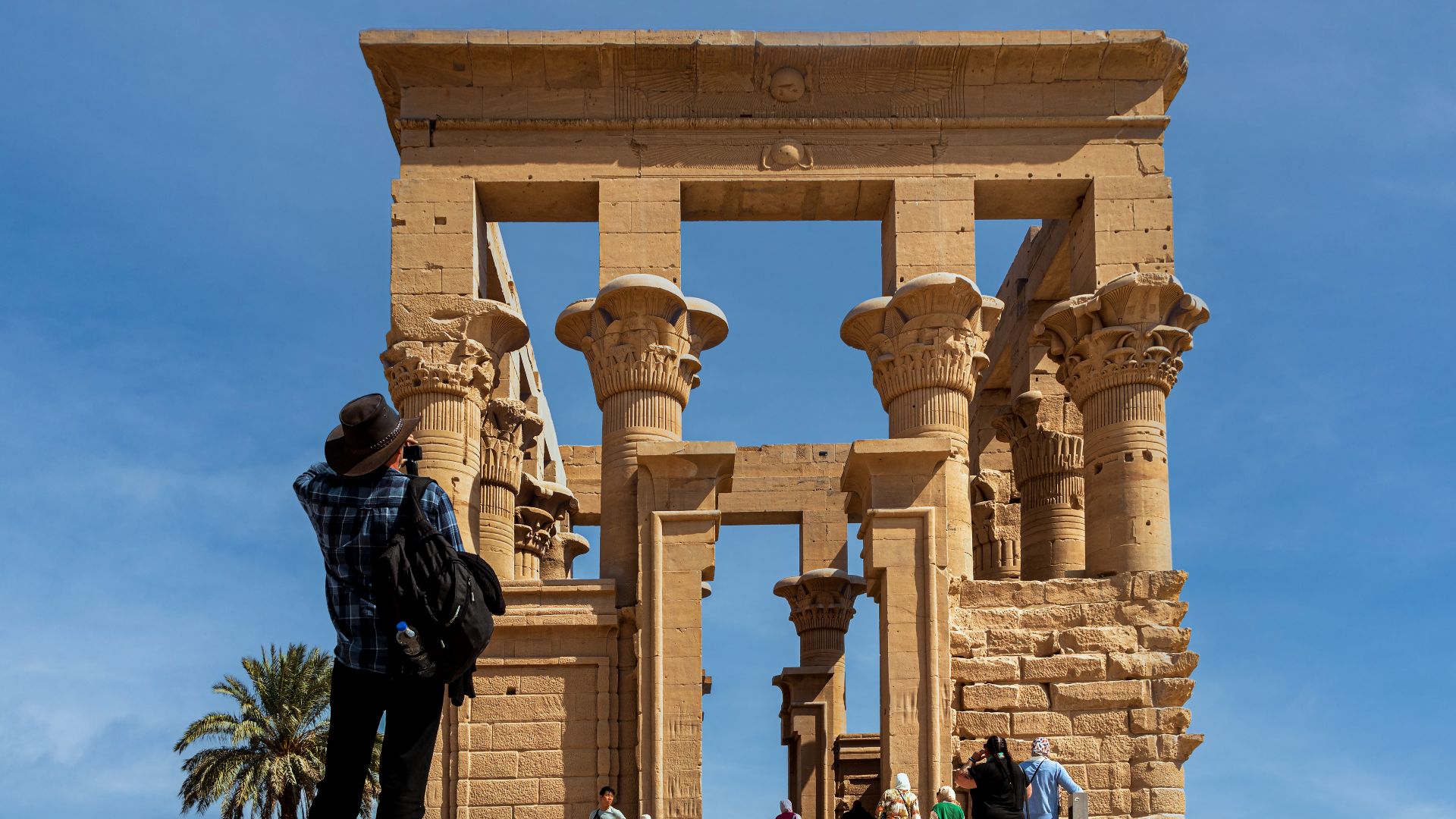 This picture was taken of a part of the Temple of Philae in Aswan, and the picture shows the beauty of the architectural details of this part of the temple and the tourists who take pictures of the temple