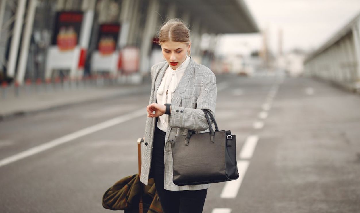 A businesswoman checks her watch while waiting at an airport terminal, looking concerned.