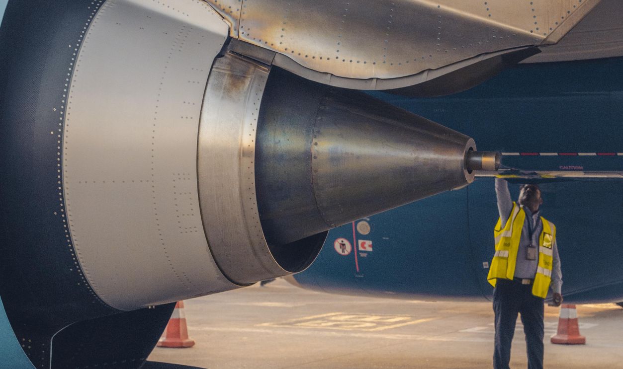 Safety officer inspecting aircraft engine at airport terminal, ensuring compliance.