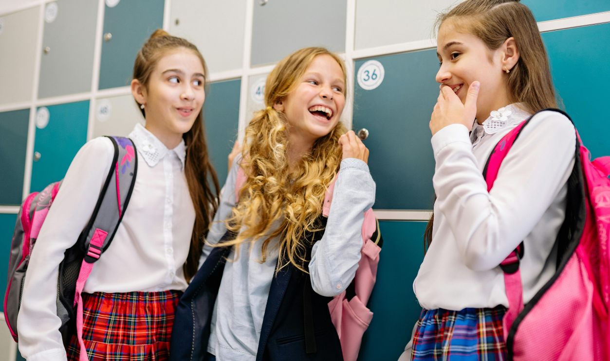 Three girls in school uniforms laughing and talking by lockers