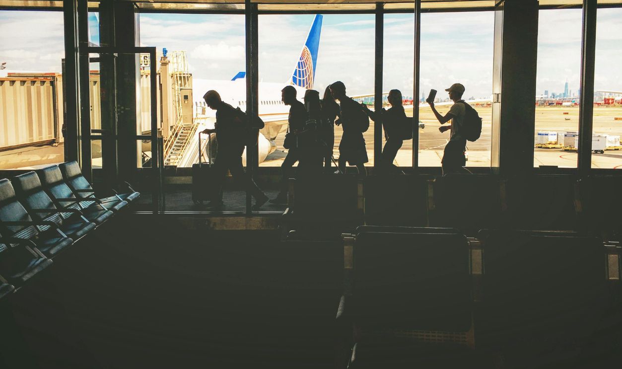 Silhouettes of travelers at an airport gate, airplane and city skyline visible through windows