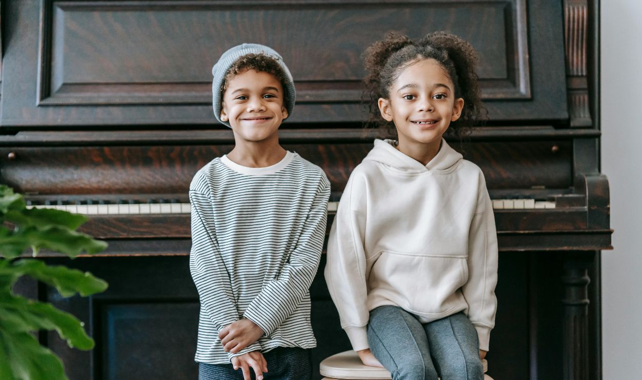 Happy siblings with a piano indoors