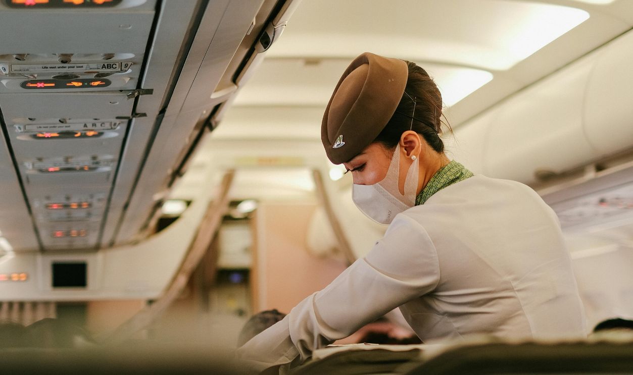 A flight attendant performs duties onboard a passenger airplane while wearing a protective mask