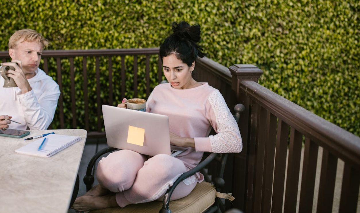 Focused woman in pink clothing working on laptop outdoors with coffee