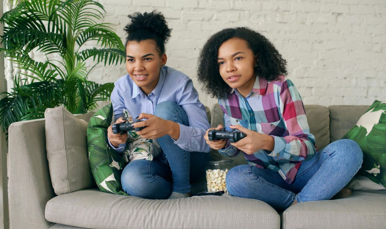 Two teenagers engaged in a video game, sitting on a cozy sofa