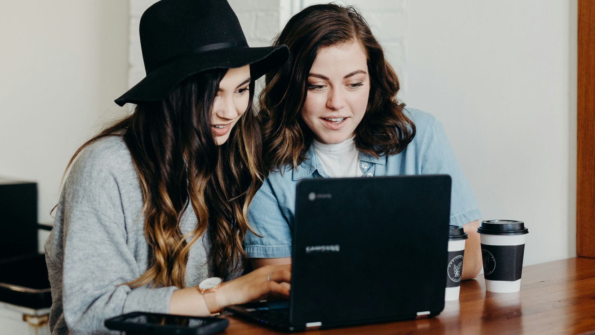 two woman sitting near table using Samsung laptop