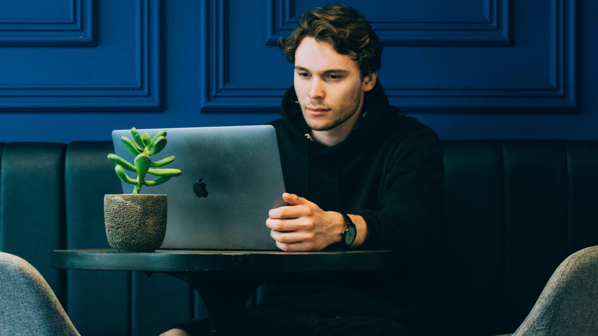 man sitting on couch with looking at his MacBook on table