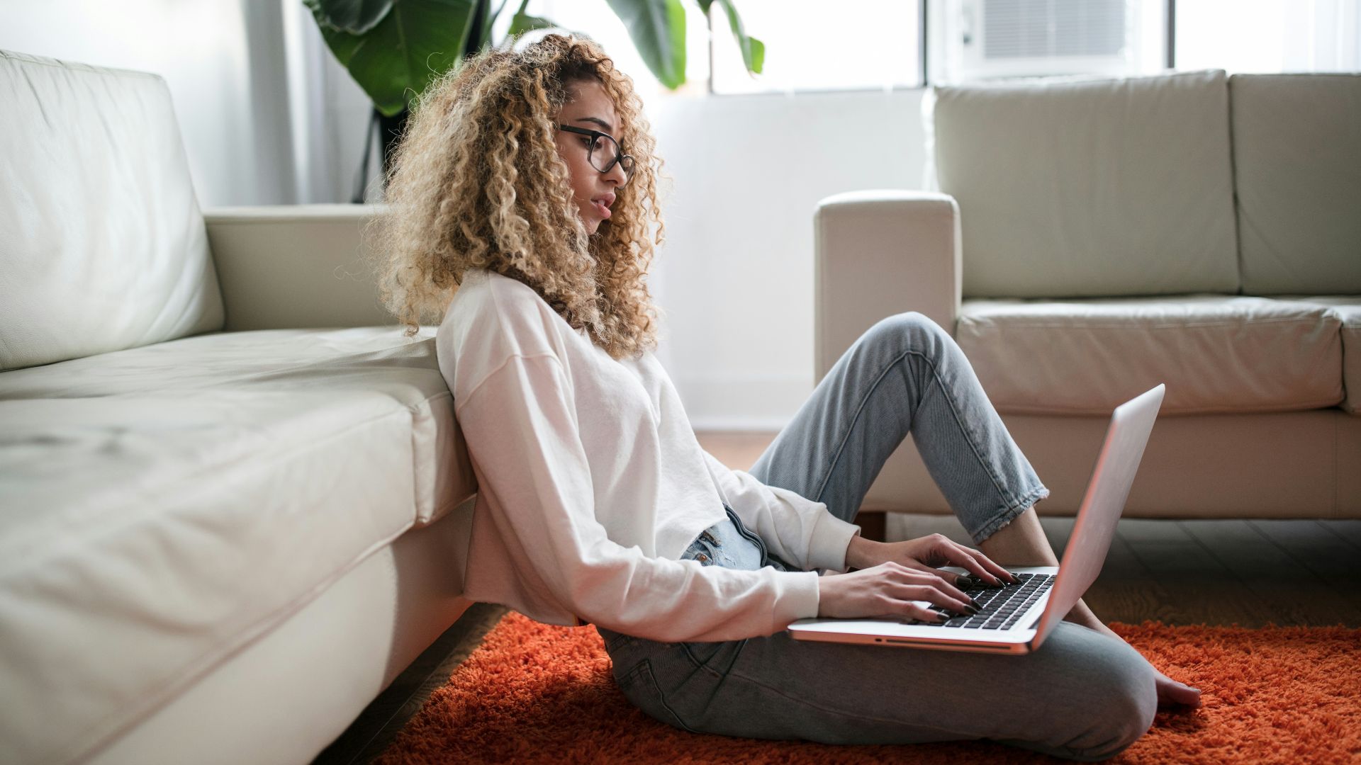 woman sitting on floor and leaning on couch using laptop