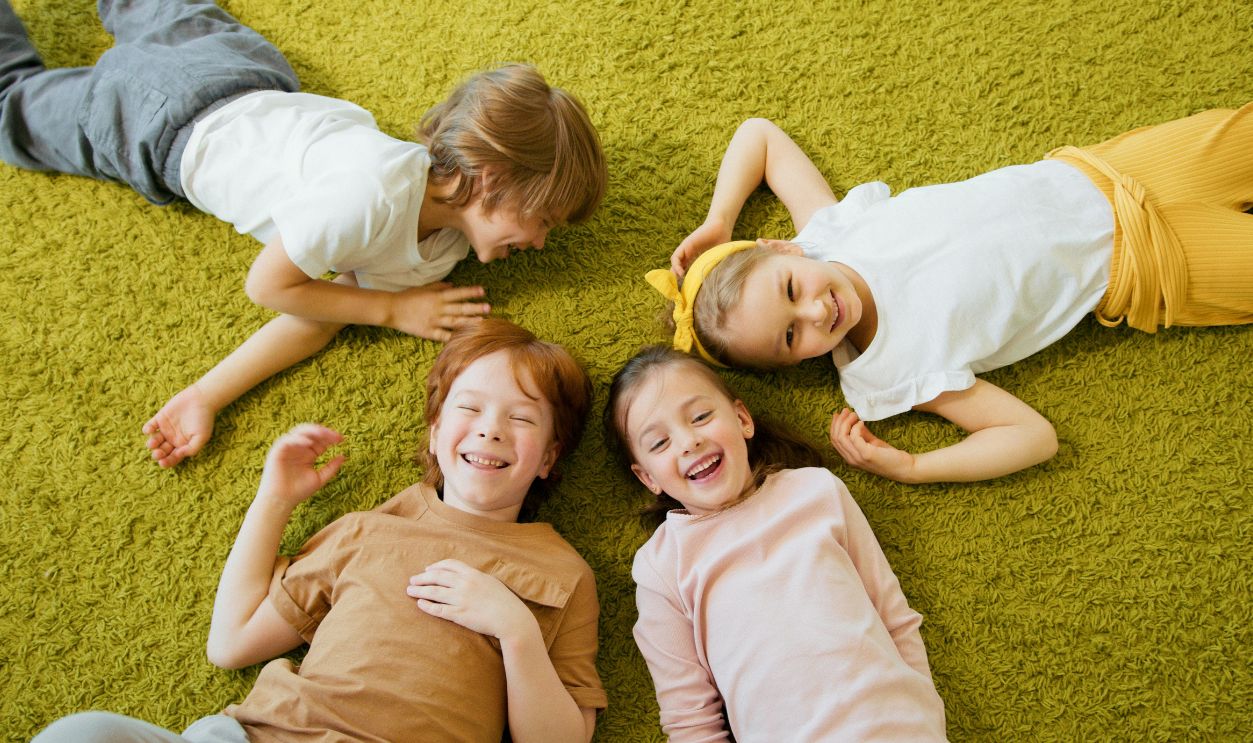 Four cheerful children lying together on a green carpet