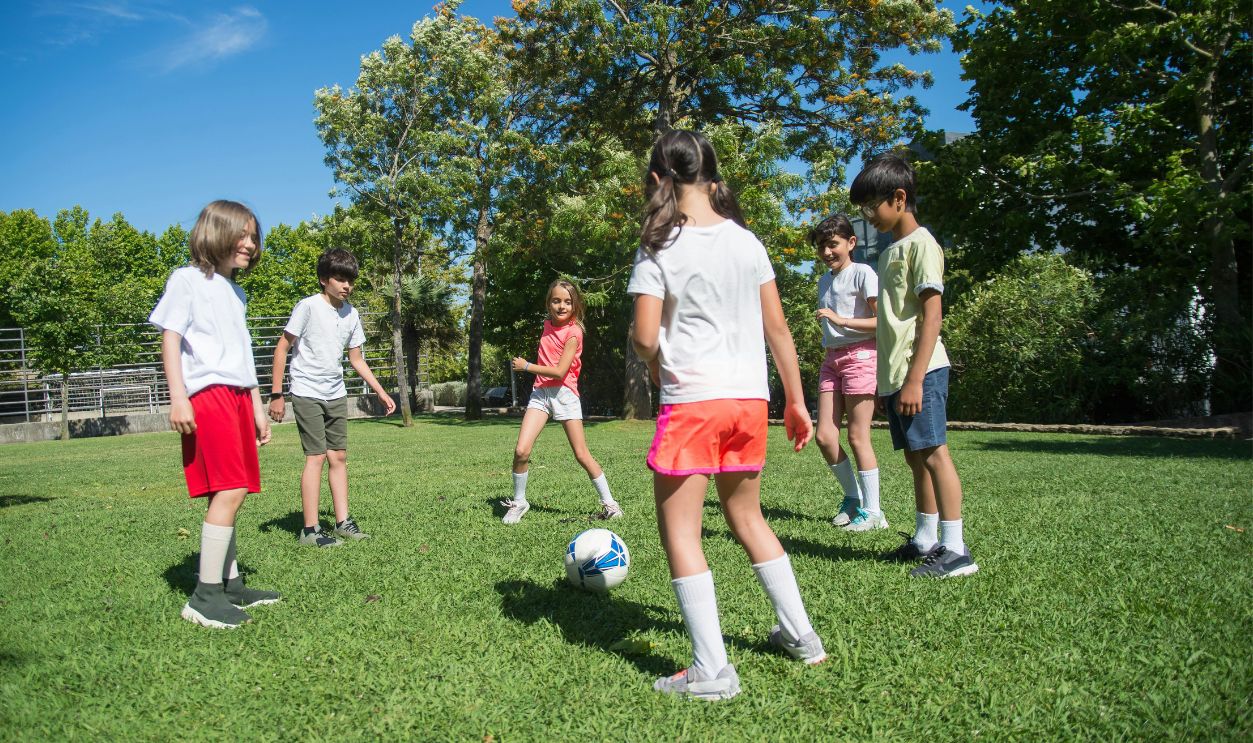 Kids play football on a sunny day in a lush, green park. 