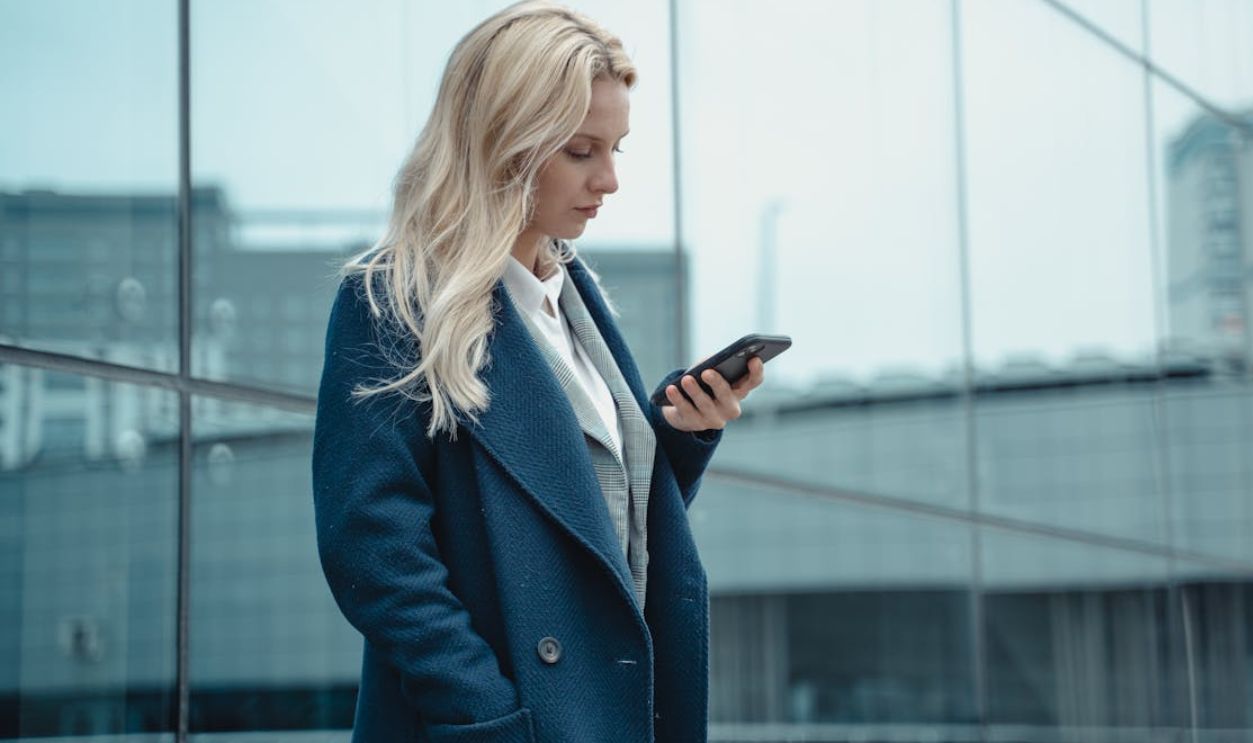 Professional woman in blue coat using smartphone outside office building