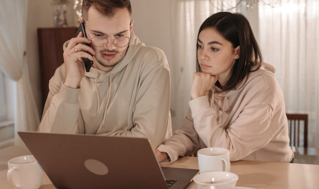 A couple in hoodies focused on work using a laptop and smartphone at home
