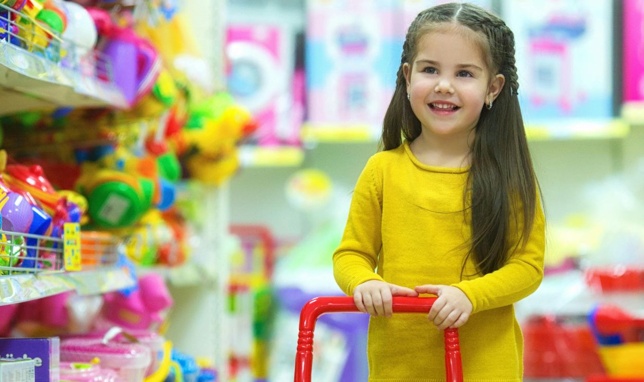 Adorable young girl happily pushing a toy shopping cart in a colorful toy store