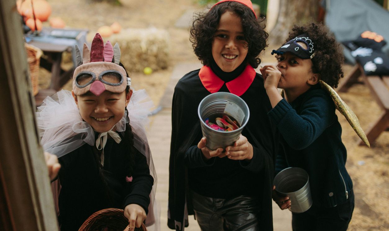 Three children in Halloween costumes joyfully trick-or-treating 