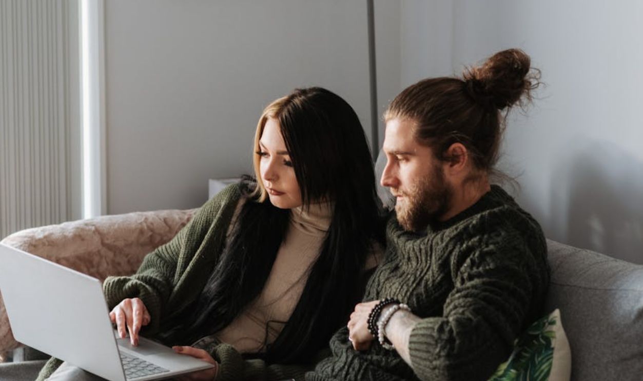 A young couple enjoys a relaxing day at home using their laptop on the couch