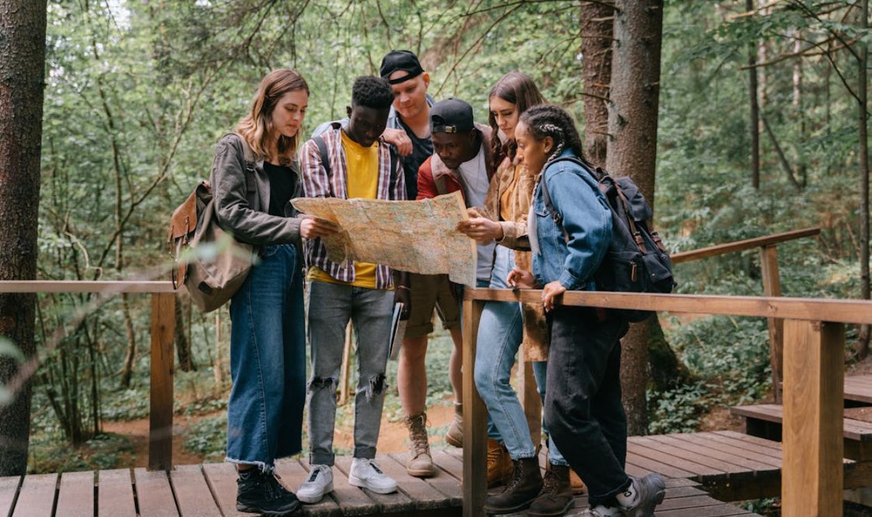 Group of young adults studying a map while hiking on a forest bridge.