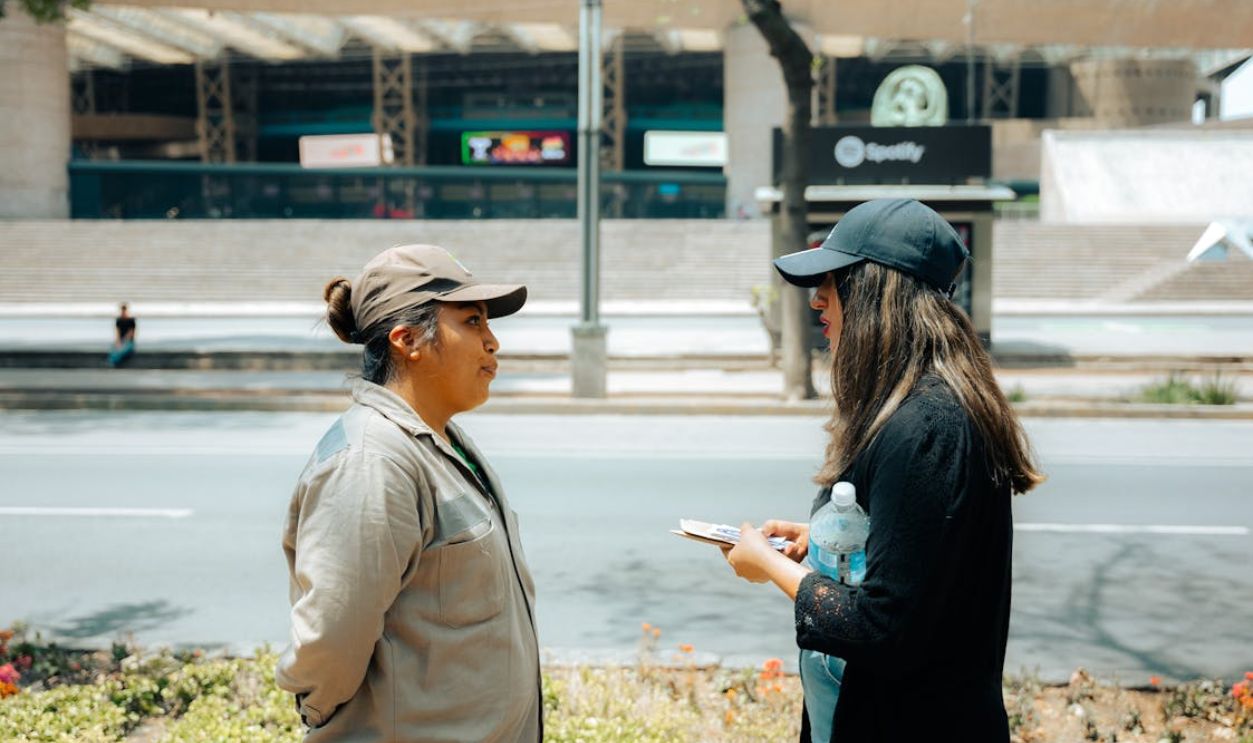Two women in conversation on an urban street with a modern building backdrop.