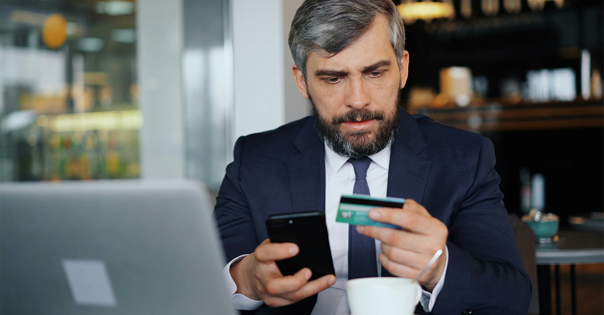 A businessman at a cafe, frowning at his credit card.