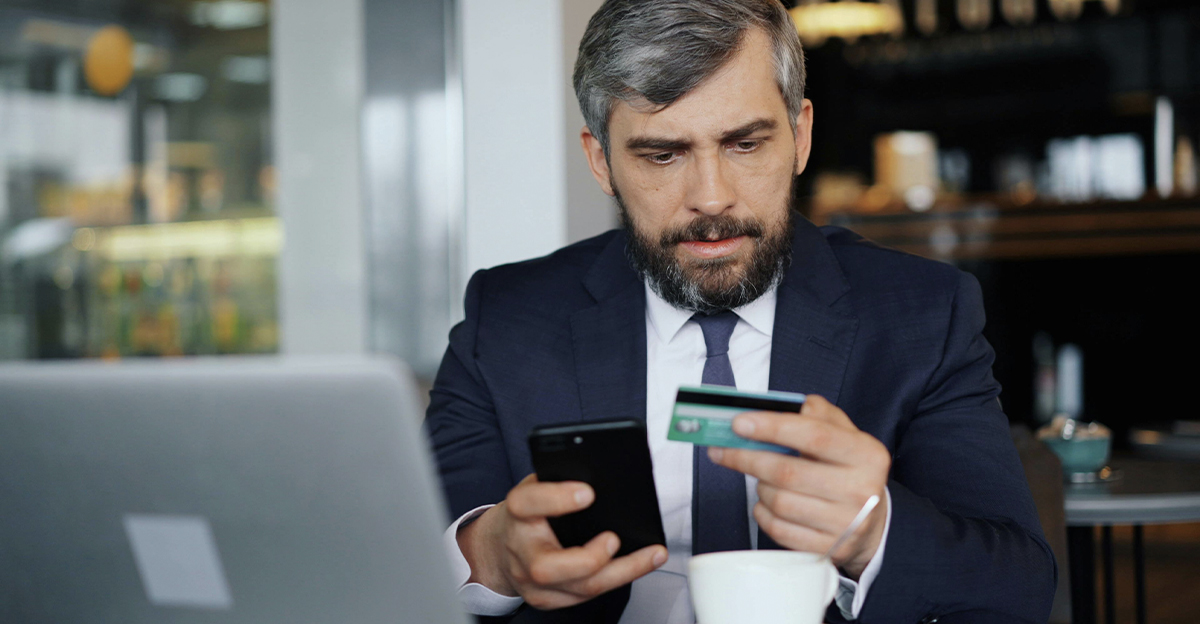 A businessman at a cafe, frowning at his credit card.
