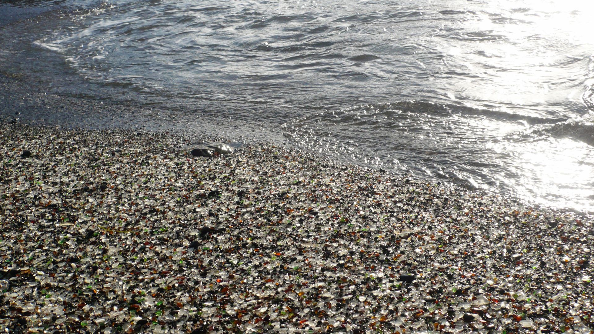 Glass Beach is a beach in  en:Fort Bragg, California that is covered in sea glass created from wave action rounding and smoothing years of glass added to the town dump into an area of coastline near the northern part of the town.  This view is of wet sea glass  as the tide was going out.