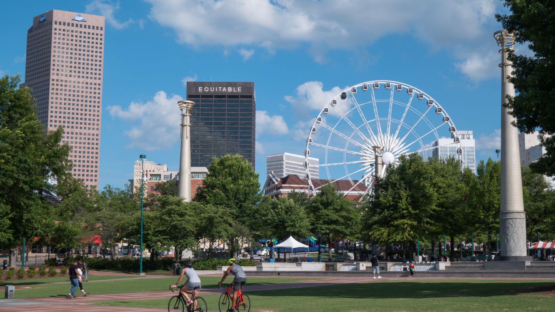 Cyclists passing through Centennial Olympic Park in downtown Atlanta, Georgia, with the skyline visible in the background. Landmarks include the Georgia-Pacific Tower, the Equitable Building (renamed 100 Peachtree in 2011), the SkyView Atlanta Ferris whee