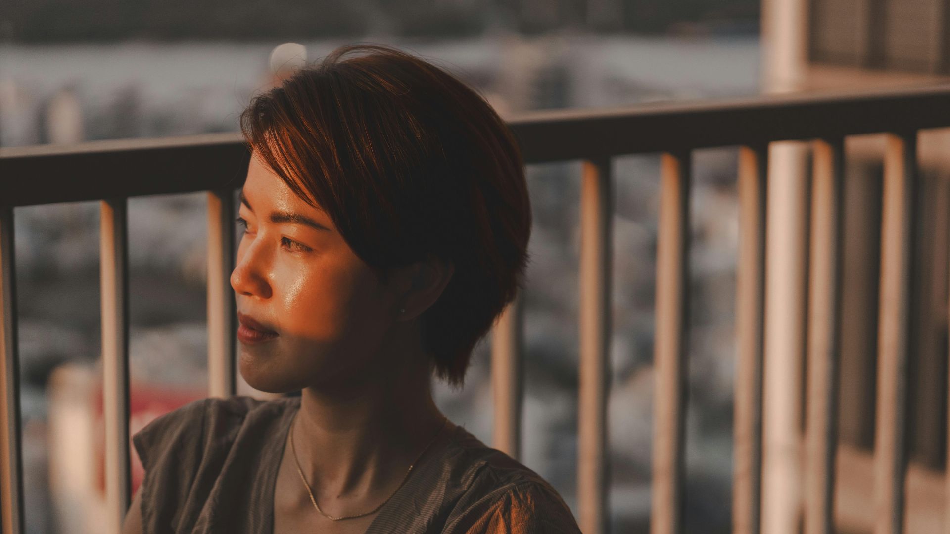 A woman gazing thoughtfully from a balcony at sunset in Ho Chi Minh City, Vietnam.
