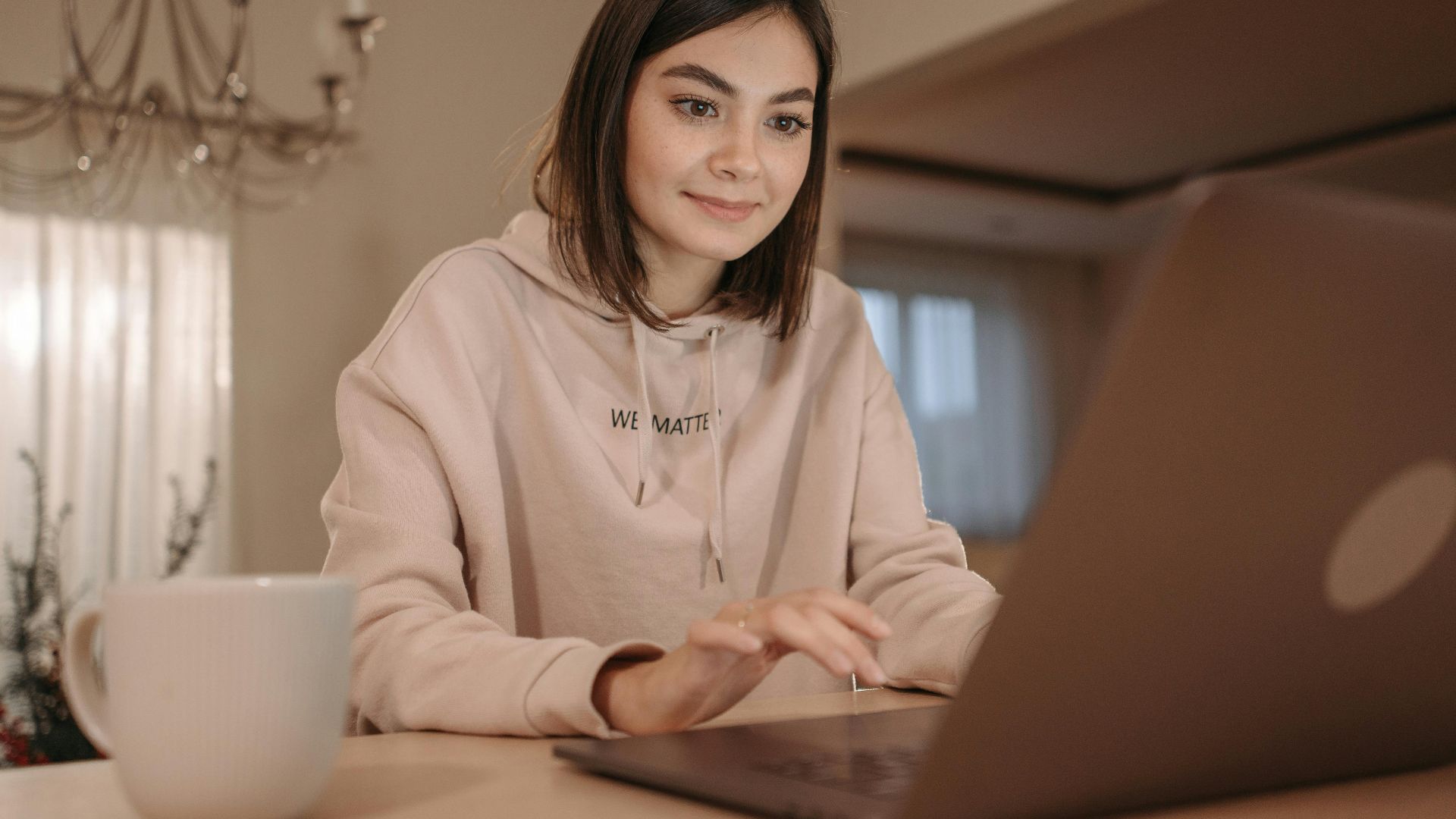 A young woman in a cozy setting using a laptop with a cup of coffee nearby.
