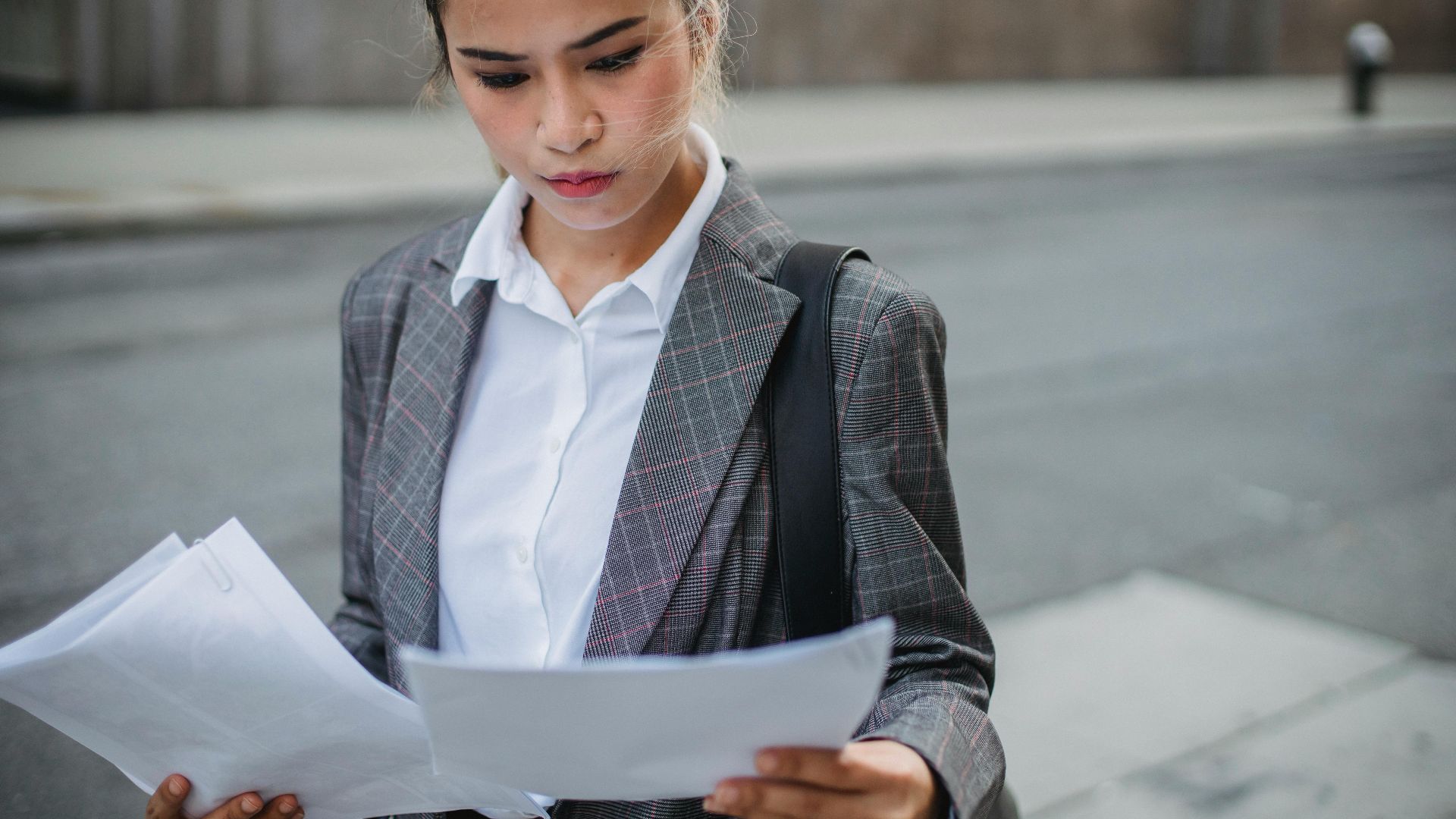 Focused businesswoman in a suit reviews important papers outdoors.