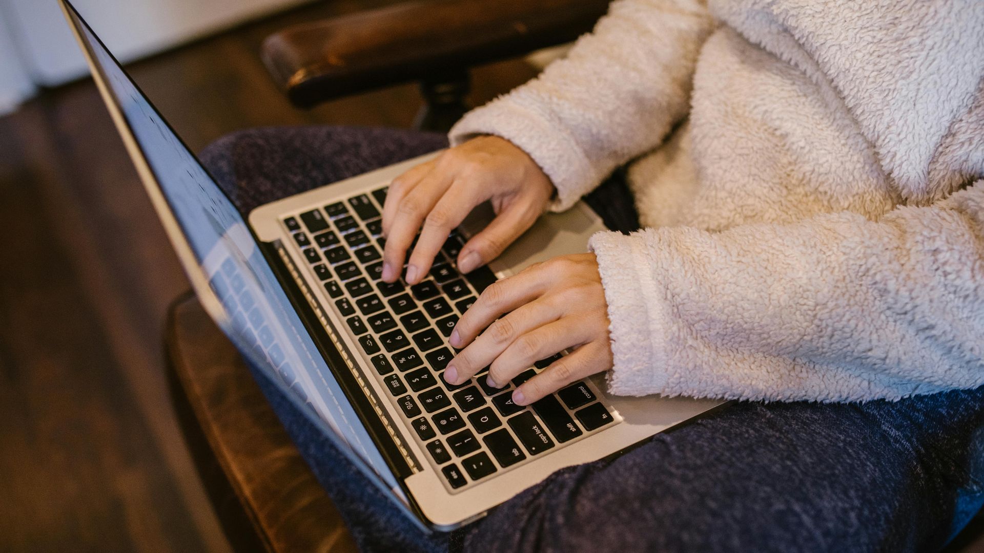 Close-up of hands typing on a laptop, wearing a warm fleece sweater, depicting home learning.