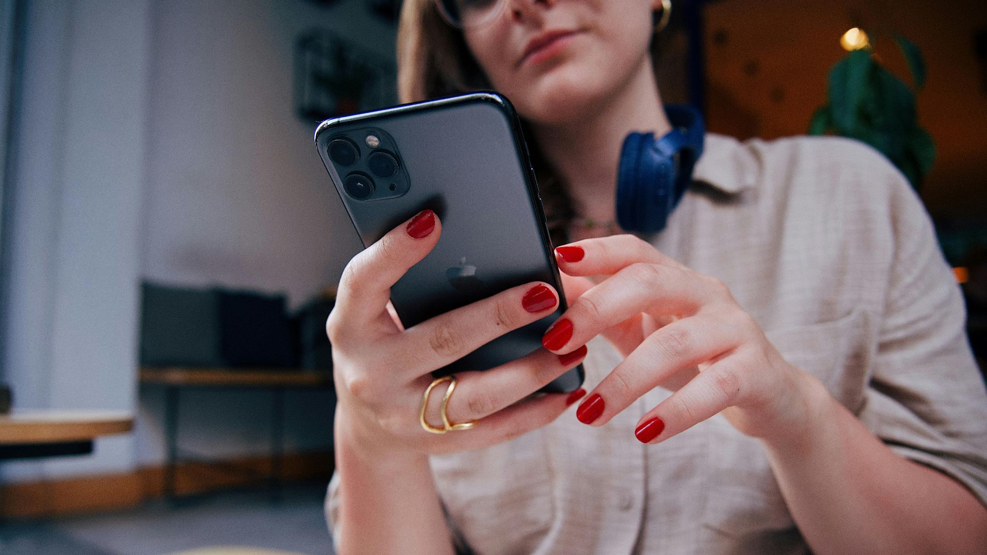 Close-up of a woman with red nails using a smartphone and headphones indoors.