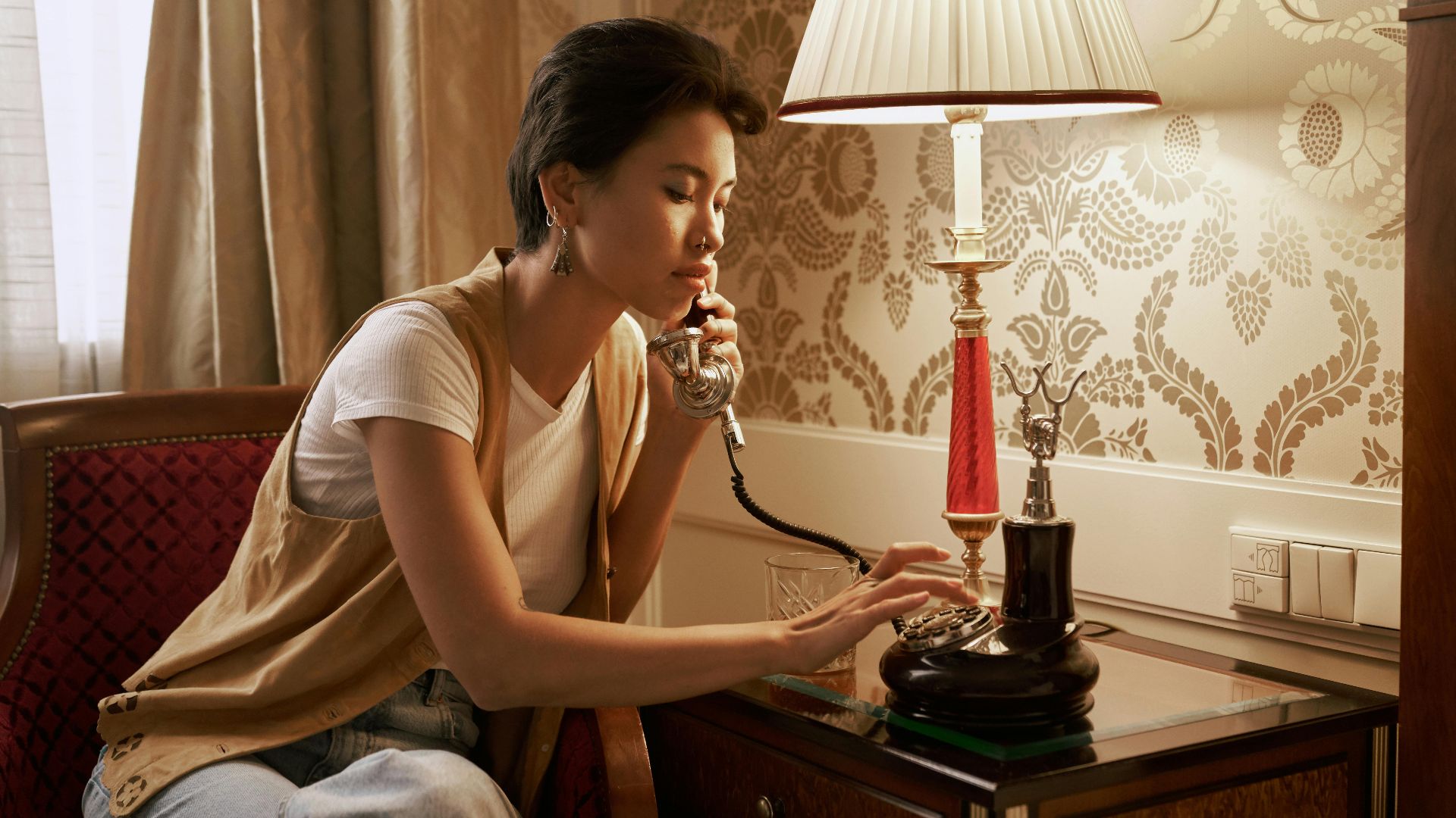 Woman speaking on vintage phone in luxurious home interior with lamp and classic decor.