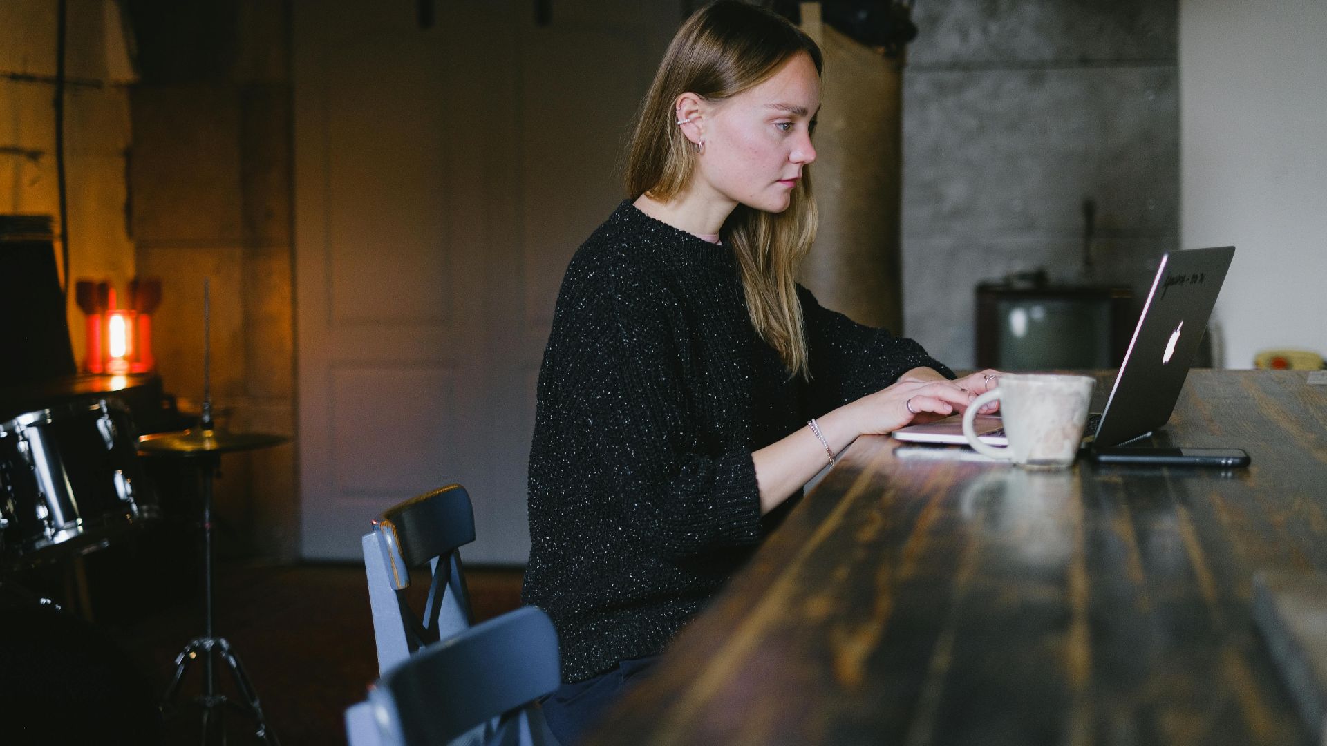 Side view of young woman working on netbook sitting at table with cup of hot beverage in kitchen