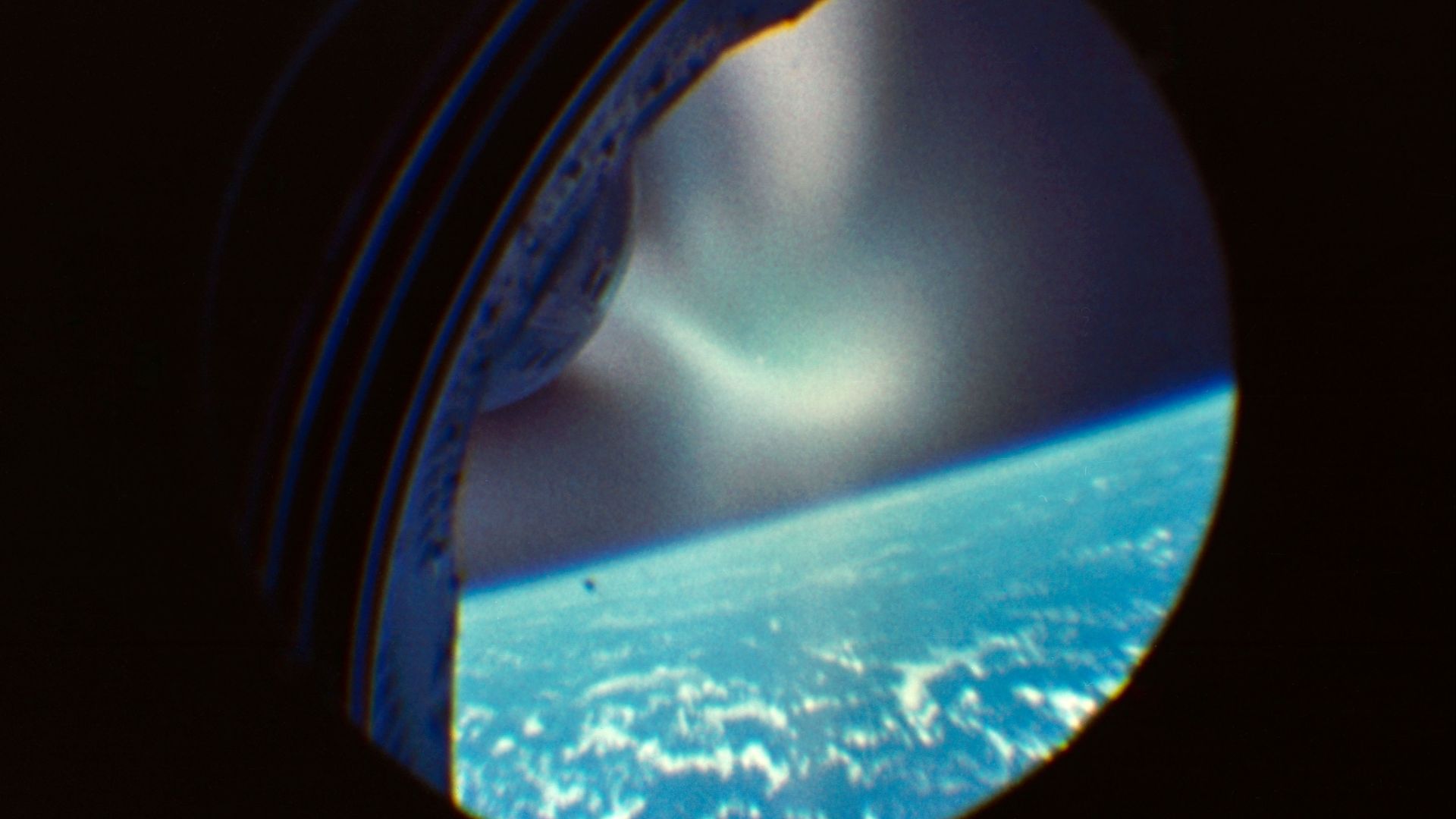 This photograph is an enlargement of a frame from a 16mm motion picture film which was mounted within the Gemini 2 spacecraft to take film through the hatch window. This scene shows the spacecraft during reentry.
