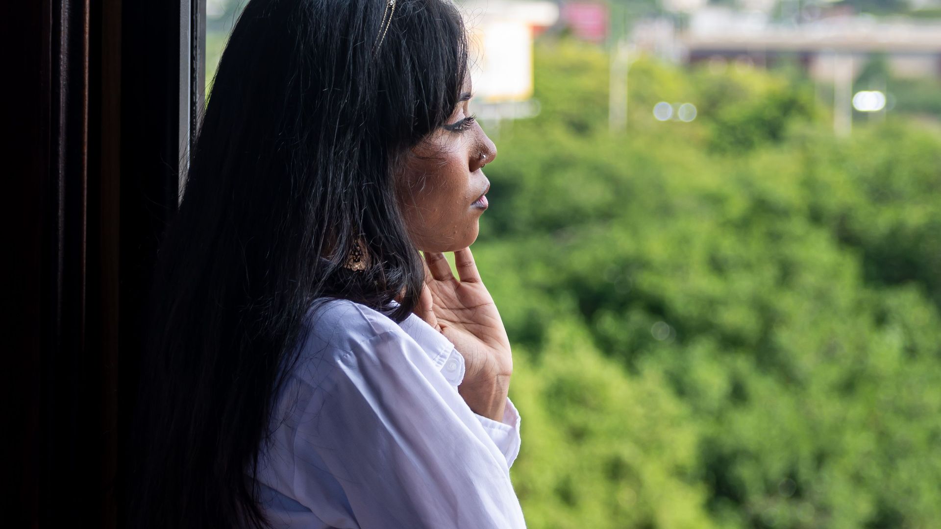 Woman in white shirt looking out a window at green hills, conveying contemplation and serenity.