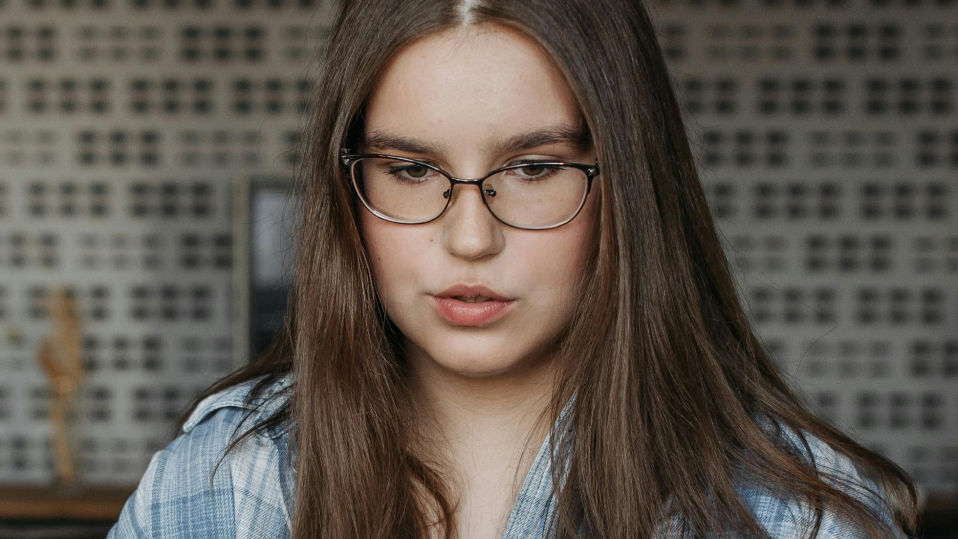 Young woman wearing glasses, engaged in work on a laptop indoors.